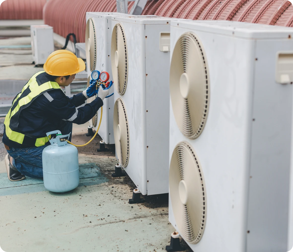 Man in a hard hat and safety vest working on an air conditioner, holding a pressure gauge in his hand