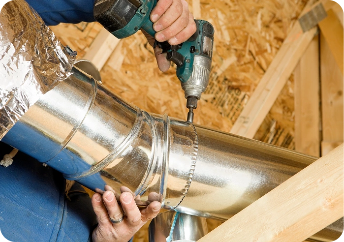Man using a drill to install a metal pipe, with wooden pieces in the background