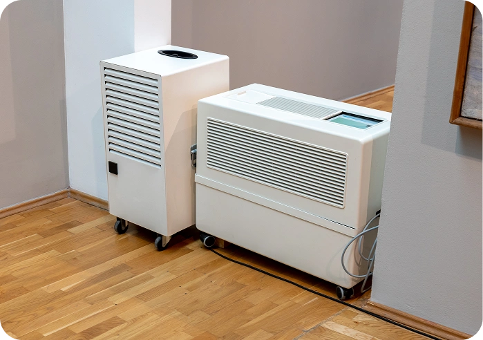 Two white air conditioners sitting on top of a wooden floor