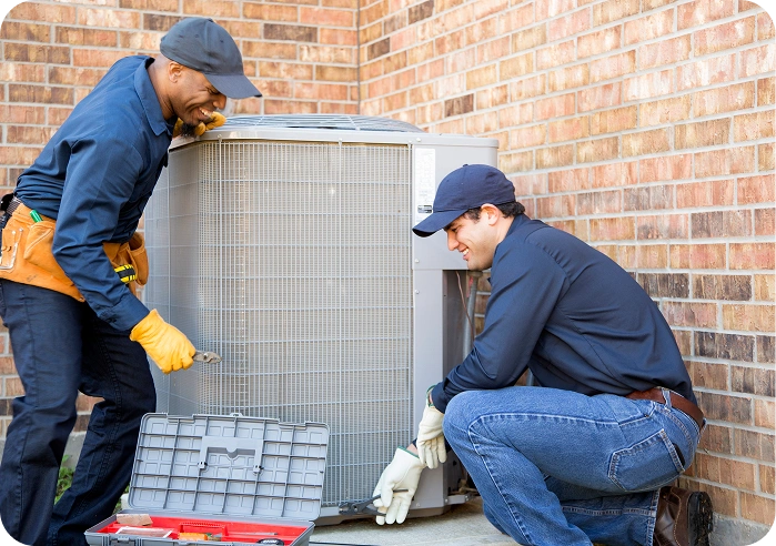 Two men working on an air conditioner in front of a brick wall